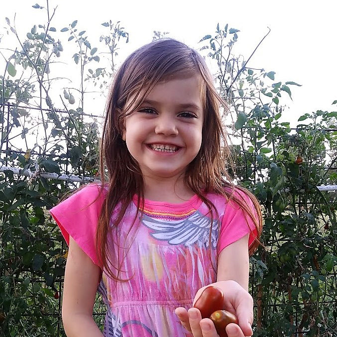 This is Tirzah, holding some tomatoes. Are those Egyptian walking onions behind her? 